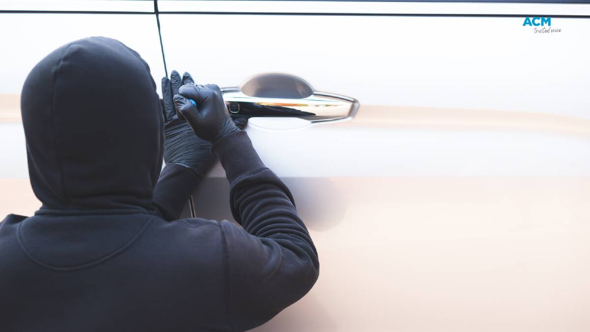 A figure in a dark hoodie breaking into a locked car. Picture via Canva